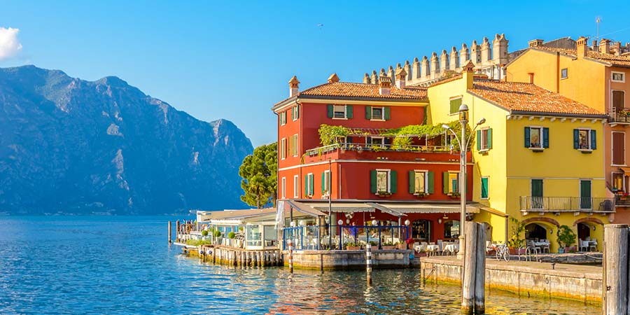 Quaint red and yellow painted houses are reflected in the shimmering blue water of Lake Garda. 