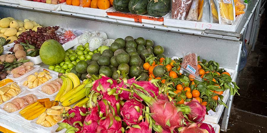 A traditional Vietnamese fruit market, bright pink dragon fruit sits next to ripe bananas and melons. 